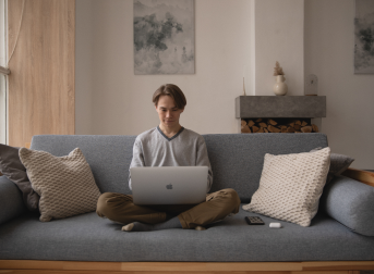 Zdjęcie przedstawiające osobe z laptopem siedzącą na kanapie